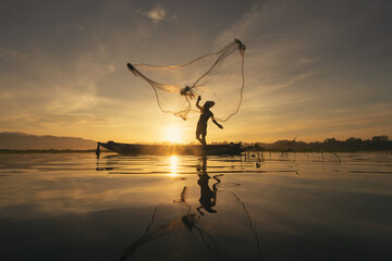 Silhouette Fisherman casting or throwing a net for catching freshwater fish in nature lake or river with reflection in morning time in Asia in Thailand. People.