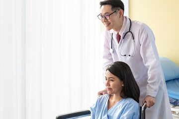 Young Doctor talking to woman in wheelchair after an operation. Smiling doctor looking at a female patient on a wheelchair in hospital. Photo of positive doctor and patient on wheelchair.