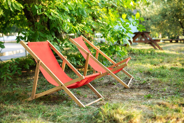 Red Deckchairs in autumn garden. Two deckchairs on summer green lawn. Lounge sunbed. Wooden garden furniture on grass lawn outdoor for relax. Backyard exterior. Garden landscape with chairs in nature.