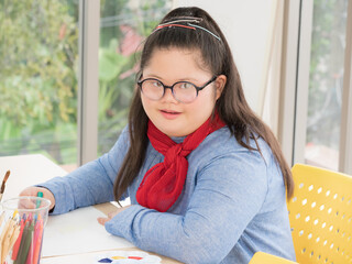 Portrait of cute down syndrome girl looking at the camera and smiling while enjoying development exercises at home..