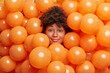 Photo of attractive curly haired woman surrounded by inflated balloons smiles gently poses at camera. Happy dark skinned Afro American lady waits for birthday party. Holiday and celebration concept