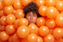 Surprised Birthday Girl Poses Over Inflated Orange Party Balloons Stares Bugged Eyes Expresses Great Wonder Or Surprise. Young Afro American Woman Enjoys Anniversary Event Has Shocked Expression