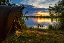 Fishing Adventures, Carp Fishing. Angler, At Sunset, Is Fishing With Carpfishing Technique. Camping On The Shore Of The Lake.Carp Fishing Sunset