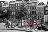 Fototapeta Uliczki - A picture of a red bike on the bridge over the channel in Amsterdam. The background is black and white. 