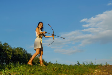 portrait of a young beautiful woman in a white tunic with a Golden belt with a bow in the image of the ancient Greek goddess Artemis