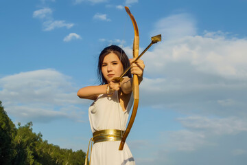 Portrait of a young beautiful girl in the image of the Roman goddess Diana in a white tunic with a bow