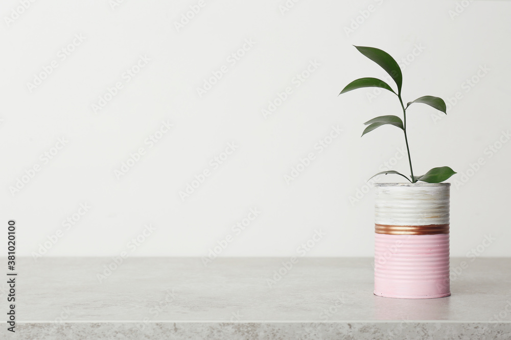 Beautiful houseplant in color tin can on light grey stone table. Space for text - obrazy, fototapety, plakaty 