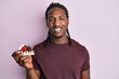 © Krakenimages.com - African american man with braids holding chocolate cake looking positive and happy standing and smiling with a confident smile showing teeth