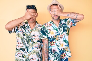 Young gay couple of two men wearing summer hat and hawaiian shirt covering eyes with hand, looking serious and sad. sightless, hiding and rejection concept