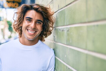 Young handsome hispanic man smiling happy leaning on the wall at street of city