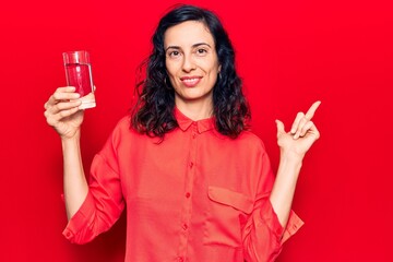 Wall Mural - Young beautiful hispanic woman drinking glass of water smiling happy pointing with hand and finger to the side