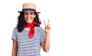 Wall Mural - Middle age beautiful woman wearing casual striped t shirt and summer hat smiling with happy face winking at the camera doing victory sign. number two.