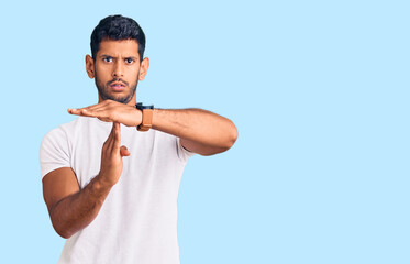 Young latin man wearing casual clothes doing time out gesture with hands, frustrated and serious face