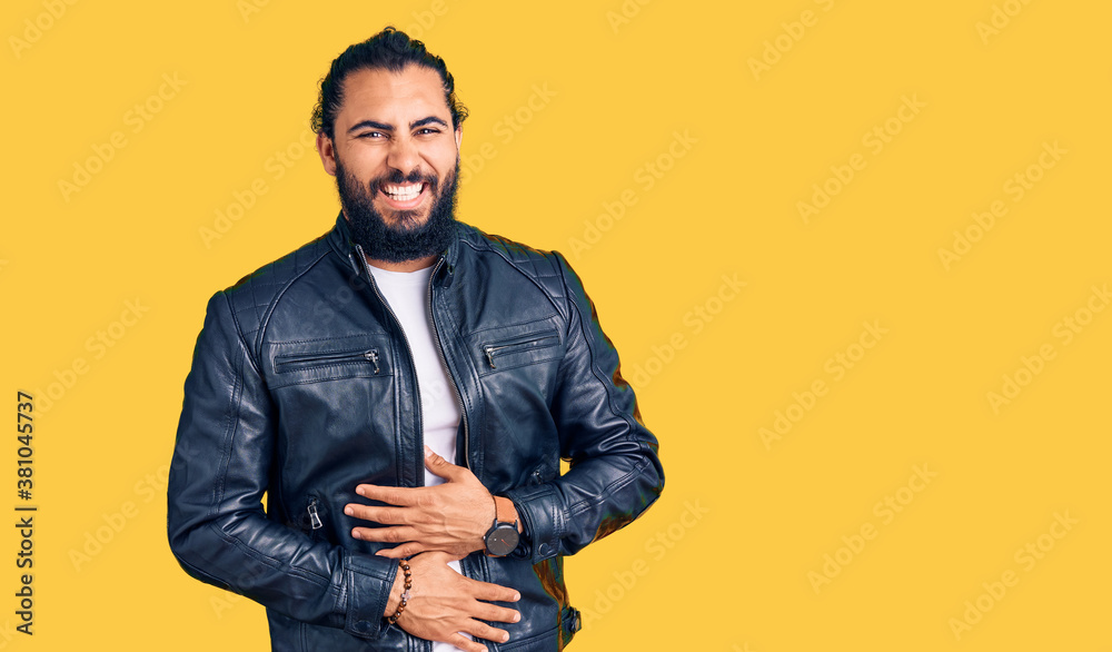 Young arab man wearing casual leather jacket smiling and laughing hard out loud because funny crazy joke with hands on body.