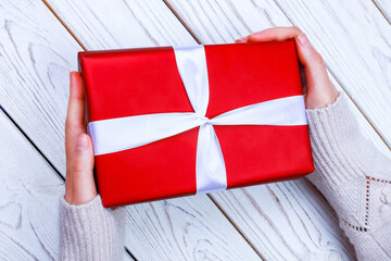 female hands holding red gift box with ribbon on wood background. Present for birthday, valentine day, Christmas, New Year.