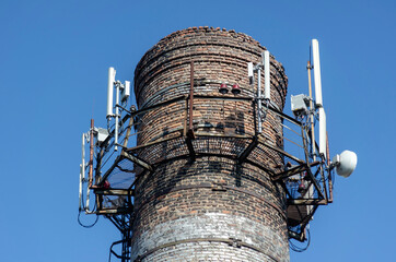 An old brick factory chimney with various antennas.