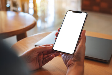 mockup image of a woman holding mobile phone with blank white desktop screen with laptop on the tabl