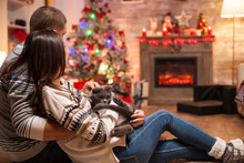 Romantic Couple With Scottish Fold Enjoying Christmas In Front Of Warm Fireplace.