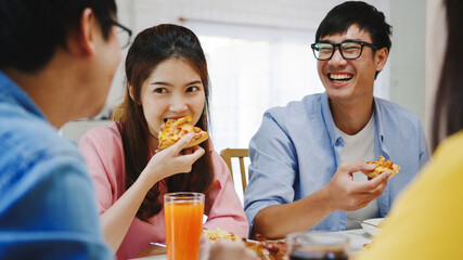 Happy young friends group having lunch at home. Asia family party eating pizza food and laughing enjoying meal while sitting at dining table together at house. Celebration holiday and togetherness.