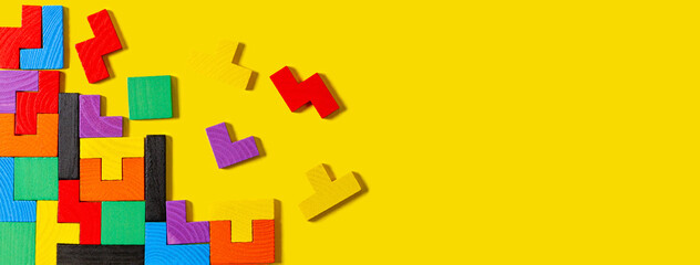 Different colorful shapes wooden puzzle blocks on yellow background. Geometric shapes in different colors, top view