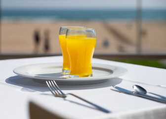 Glass of fresh orange juice on the beach background. Two glasses of orange juice on a white plate. Shallow depth of field