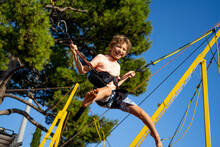 Children Have Fun Jumping On Bungee Trampoline Secured With Rubber Bands. Sunny Day