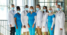 Mixed-races team of specialists, males and females doctors in hospital. International group of medics in medical masks. Protected workers. Multi ethnic physicians and nurses in uniforms in clinic.