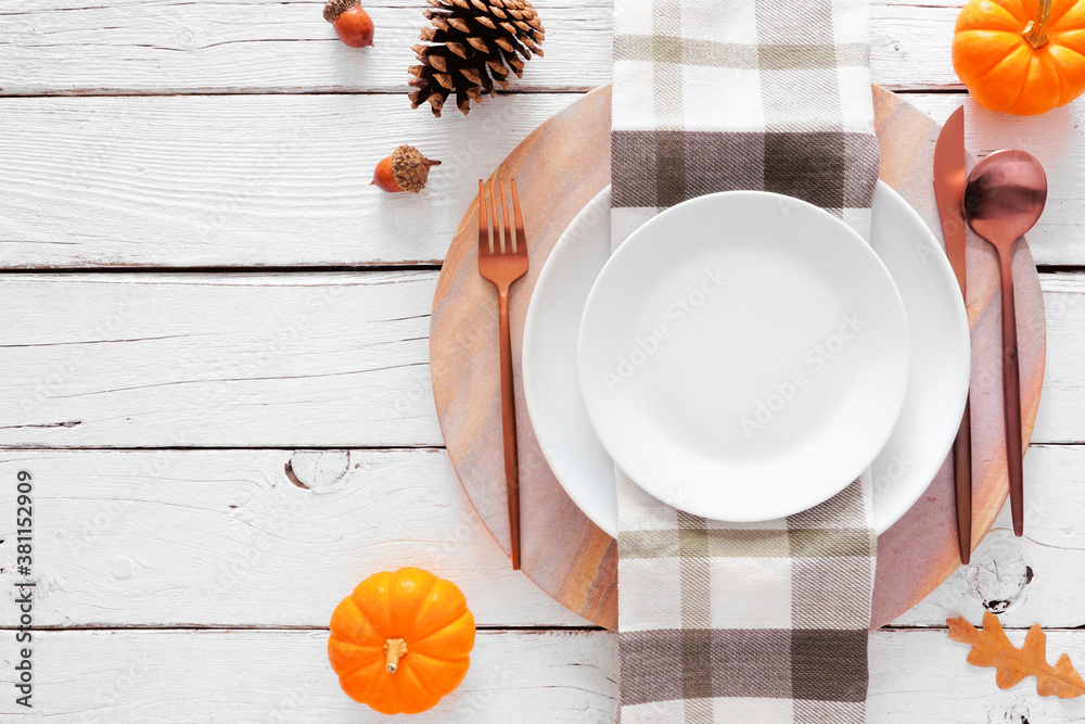 Autumn harvest or thanksgiving dinner table setting with plate, flatware, check print napkin, pumpkins and decor. Top view on a white wood background. - obrazy, fototapety, plakaty 