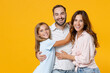 © ViDi Studio - Laughing young happy parents mom dad with child kid daughter teen girl in basic t-shirts hugging looking camera isolated on yellow background studio portrait. Family day parenthood childhood concept.