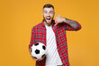 Excited young man football fan in red shirt cheer up support favorite team with soccer ball doing phone gesture says call me back isolated on yellow background studio. People sport leisure concept.