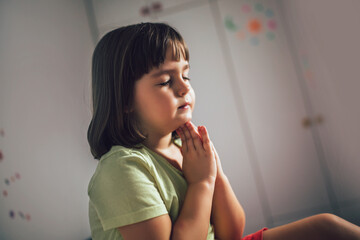 Cute little girl praying at home