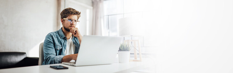 Young man typing on laptop. Modern businessman at sunny office. Freelancer at work. Blogger or journalist writing new post