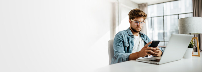 Young man with smartphone in his hands. Modern businessman at sunny office. Freelancer at work.