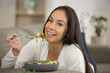 young woman eating healthy salad on sofa at home