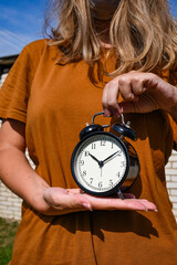 Wall Mural - Woman in brown t-shirt holding alarm clock in hand. Lost time concept. Business idea. Lifestyle