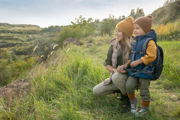 Poster - Young cheerful blond woman and her cute little son with backpack on trip