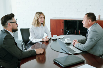 Subordinates in formalwear sitting by table in boardroom in front of director