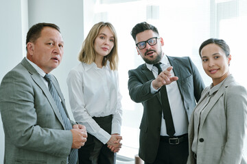 Poster - Confident mature businessman pointing forwards while standing among colleagues