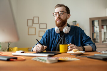Wall Mural - Young creative freelance designer having drink while holding stylus over tablet
