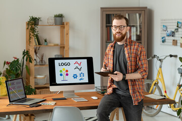 Wall Mural - Cheerful freelance designer holding stylus over tablet while sitting on table