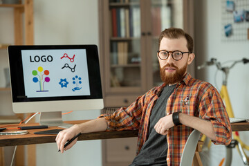 Wall Mural - Successful male designer sitting on chair by table with computer monitor