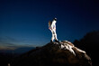 Full length of spaceman reaching the top of rocky hill with beautiful blue sky on background. Astronaut wearing white space suit with helmet. Concept of space exploration by human race.