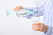 © Pixel-Shot - Woman pouring water from bottle into glass on light background
