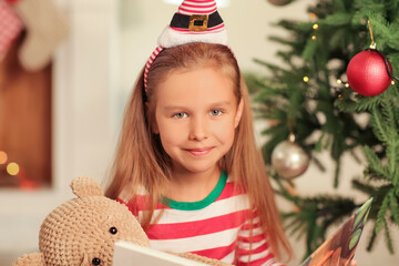 Poster - Cute little girl reading book at home on Christmas eve