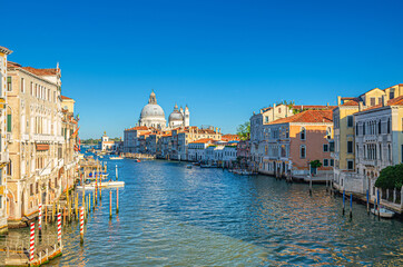 Venice cityscape with Grand Canal waterway Canal Grande in historical city centre. Santa Maria della Salute Roman Catholic church on Punta della Dogana, blue sky background. Veneto Region, Italy.