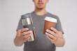 zero waste and eco friendly concept - young man comparing thermo cup with disposable paper coffee cup over grey background