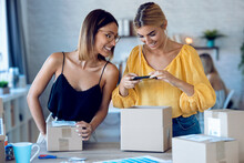 Two Beautiful Freelance Business Women Using Smart Phone To Taking Photos To Sell Online While Preparing Pack Product Box In Her Startup Small Business.
