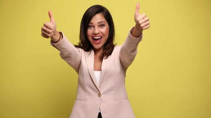 Wall Mural - beautiful businesswoman smiling at the camera and giving a thumbs up with both her hands on yellow background