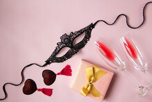 A Lace Mask For A Woman, Red Tassels Burlesque Patties, A Gift Box With Bow, Glasses Of Wine On A Pink Background. Sexy Toys For Adult Games. Flat Lay, Top View.
