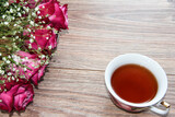 Fototapeta Lawenda - A Cup of tea with roses on a wooden background.